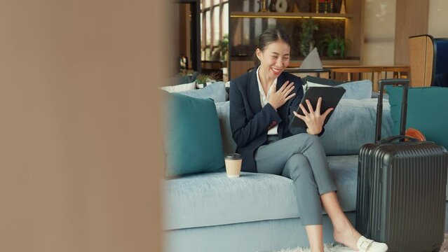 Youth Asia Female passenger formal suit sit on sofa couch training online meeting on digital tablet in airline lounge wait airplane transit international airport. Hotel Travel business trip concept.