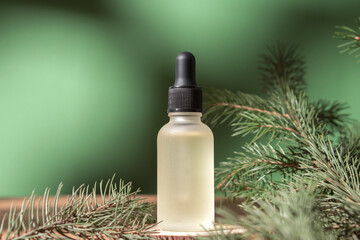 Cosmetic bottle with essential oil on green fir tree background. Beauty product for facial skin care, bottle for branding of medicine or cosmetics. Natural organic cosmetics