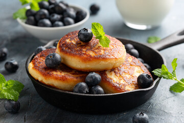 Cottage cheese pancakes served in cast iron frying pan with blueberries and mint leaves. Healthy breakfast food.