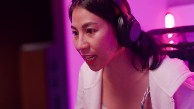 Close-up Young Asia female sit on gaming chair wear headset focus concentration pc screen competition tournament championship in game room at house. Gamer girls raise fist gloats over winning e sport.