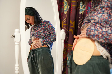 young woman looking in the mirror at her ostomy bag. colon cancer awareness