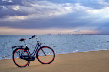 Obraz premium Port building from harbour in Rotterdam. Ladies bike on the beach in depth blur. Landscape of North Sea water and sand after sunrise under moody sky. Netherlands, South Holland, Goeree-Overflakkee.