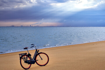 Fototapeta premium Port building from harbour in Rotterdam. Ladies bike on the beach in depth blur. Landscape of North Sea water and sand after sunrise under moody sky. Netherlands, South Holland, Goeree-Overflakkee.