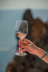 A female hand holds a glass of wine against the background of the sea and mountains.