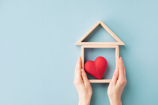 Womans hands holding model of wooden house with red heart for happy family. Real estate, sweet home, housewarming, mortgage and buy new property concept.