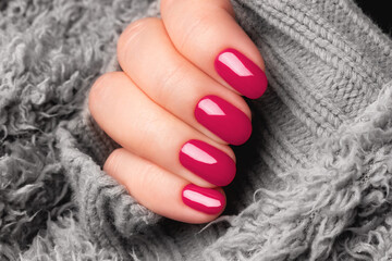 Female hand with beautiful manicure - viva magenta nails on gray fluffy knitted fabric. Nail care concept