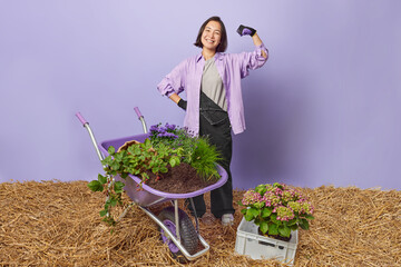 Home gardening and planting flowers concept. Positive strong Asian female gardener shows muscles...