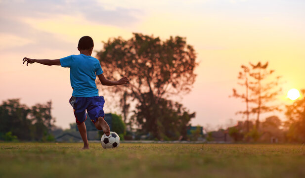 An action sport of a group of kids playing soccer football for exercise in community rural area under the sunset. picture with copy space for digital detox activity for children.