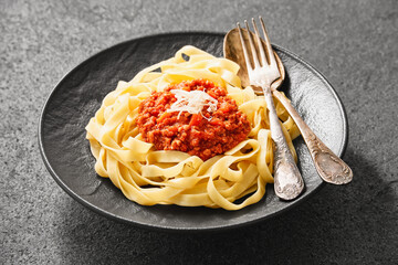 Close-up of a plate of fresh tagliatelle pasta with bolognese sauce on a gray background. High angle view.