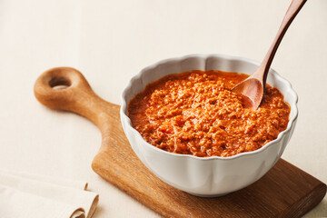 A bowl of fresh BOLOGNESE SAUCE on a wooden cutting board on a linen tablecloth. High angle view.