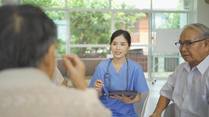 An Asian nurse talking to a group of old elderly patient or pensioner people smiling, relaxing, having fun together in nursing home. Senior lifestyle activity recreation. Retirement. Health care