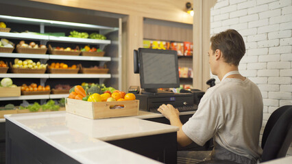 Fototapeta premium Portrait of a caucasian man working on cashier in a supermarket or retail shop, snacks and food on grocery products shelves. Food shopping. People lifestyle. Checkout business counter service. Worker