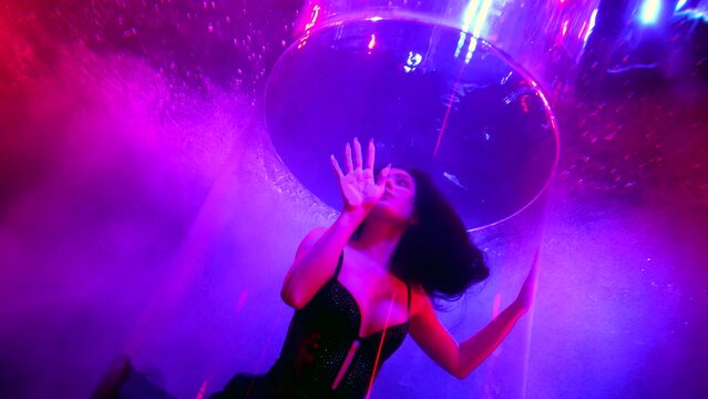 beautiful woman with long dark hair swimming in pool with glass tube and colored lights, underwater
