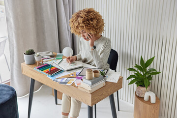 Inspired female designer draws sketches in album poses at workplace with crayons stationary tablet...