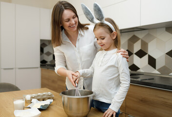 Mother and daughter in bunny ears preparing and whisking dough in modern kitchen. Time for being together