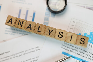 Word analysis collected from wooden cubes with magnifying glass and pen on financial report.