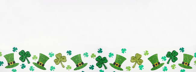 St Patricks Day shamrock and green leprechaun hat bottom border. Top view over a white banner background with copy space.