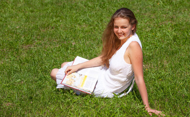 happy female student sitting on the grass with a book