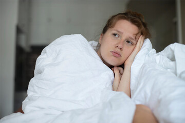 Portrait of young unhappy depressed girl, beautiful lazy lonely woman covering herself in blanket, suffering from depression with sad upset frustrated look at home in living room in early morning