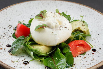Salad with farmer's burrata, ripe Brazilian avocado, juicy tomatoes, balsamic cream and olive oil in a plate. Selective focus