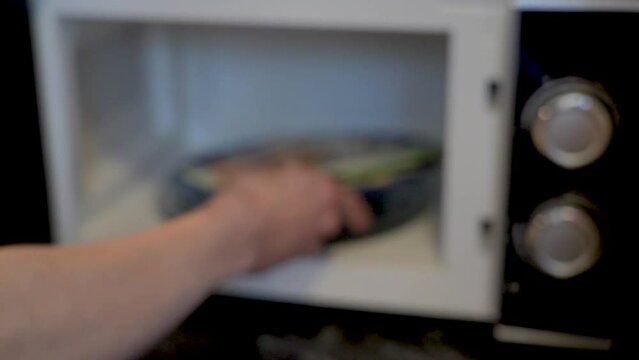 Euro banknotes on a plate in the microwave are heated and change shape when heated. A man puts a plate of European money into the oven.