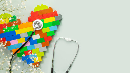 Multicolored kid bricks heart shape with stethoscope on blue background with white flowers. Health...