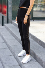 Young stylish happy brunette woman on a busy business urban street in black sleeveless top and pants. Street style photoshoot.