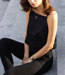 Young stylish happy brunette woman on a busy business urban street in black sleeveless top and pants. Street style photoshoot.