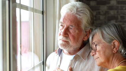 Pensive elderly mature senior man in eyeglasses looking in distance out of window, thinking of personal problems. Old woman wife consoling and hugging sad husband, copy space