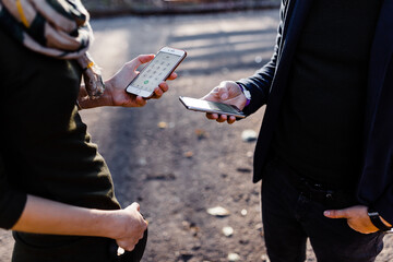 A man and a young blonde are exchanging phones in the park