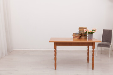 cabinet table with a stack of books and a vase of flowers chair by the table