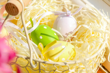 Close-up view of a rustic basket with Easter eggs on a wooden windowsill in sunlight. Easter decor