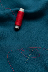 A needle with a red thread on a blue fabric. Close-up.
