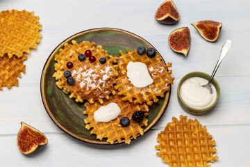Waffles with yogurt and berries on a green plate. Yogurt in a bowl, waffles and figs on the table.