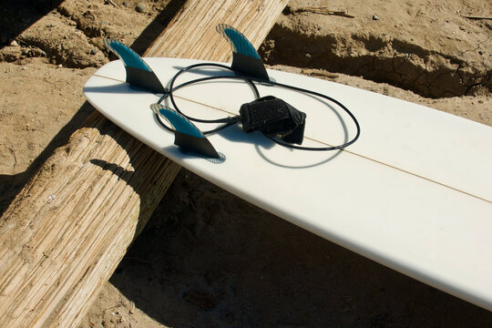 three finned surfboard resting against a log at the beach