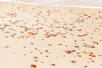 Natural stones amber yellow colored on beige sand ans sea wave. Aesthetic minimal nature scene with pebble stones on sandy background. Summer vacation or relaxation concept, selective focus