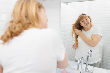 Happy young woman is combing hair in the bathroom.