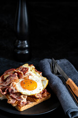 Fried eggs, bacon and toasts on black background. Breakfast concept. Selective focus.