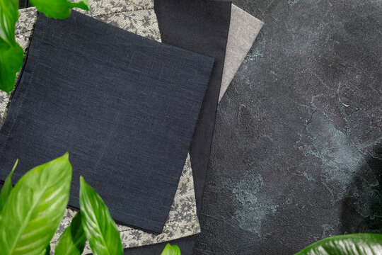 Folded black napkins on black background with green leaves and copy space. Eco friendly Mock up for display or montage of dishes, food or washing detergent. Showcase for presentation. Flat lay
