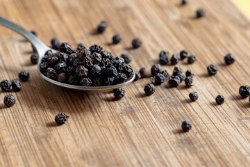 Black peppercorns on a spoon. Dried round peppers on a spoon