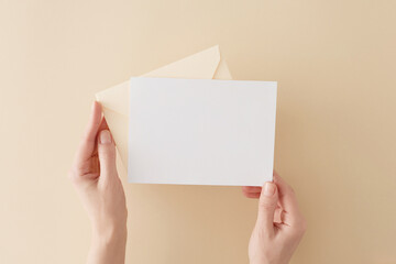 First person top view photo of female hands holding open pastel yellow envelope with white card on...