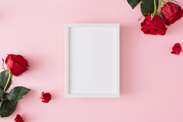Mother's day concept. Top view photo of red roses on pastel pink background and white vertical frame in the middle. 8-march holiday card idea.
