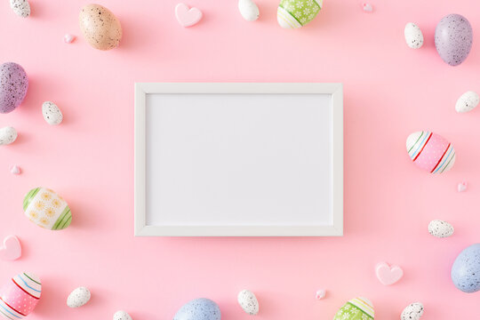 Easter composition. Flat lay photo of colorful eggs, hearts on pastel pink background and frame in the middle. Spring holiday concept.