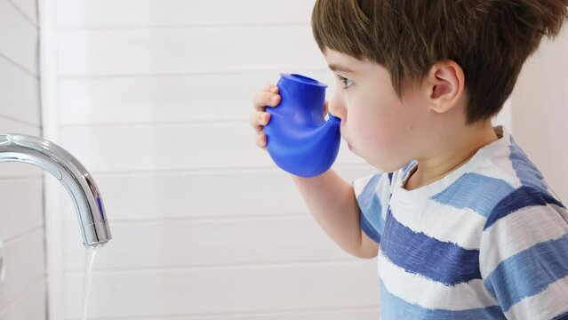 Nasal irrigation. Kid making nasal wash with saline. A young child boy uses the Neti Pot to treat runny nose. Nasal lavage. An Irrigation can. Sinus problem. Nasal allergies. Home bathroom background.