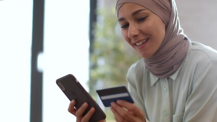 Young happy muslim woman in hijab paying online with smartphone and credit card, entering personal data in app - Powered by Adobe