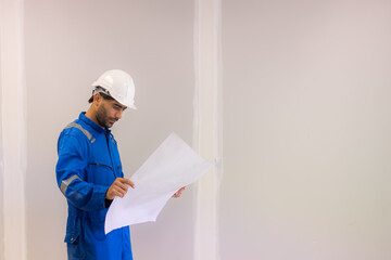 Arab civil engineer wearing safety uniforms workwear  Standing holding a blueprint of a real estate construction project to check the construction progress at the construction site.