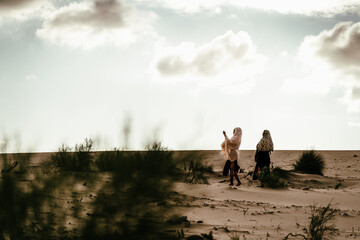 African and Caucasian girl with headscarf walking in the desert.