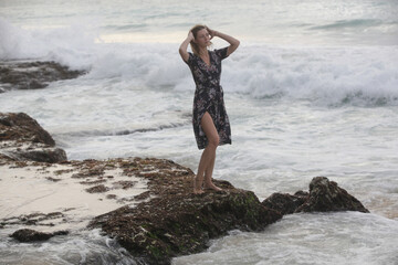 Portrait of beautiful young woman in dark floral wrap dress on wild rocky beach 