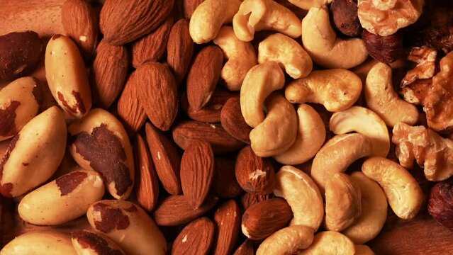 Mix with different types of nuts on a wooden rotating plate. Nuts, cashews, almonds and Brazilian nuts. Close up 4k video healthy food with proteins.