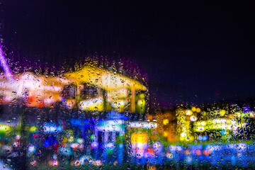 City view through a window on a rainy night,Rain drops on window with road light bokeh, City life in night in rainy season abstract background. Focus on drops on glass